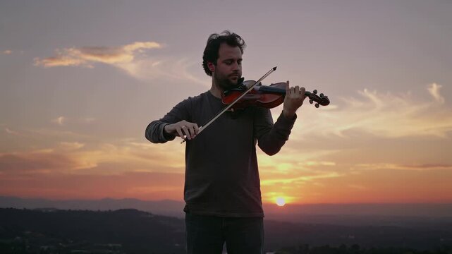 A man playing the violin outdoors during a scenic sunset evening.