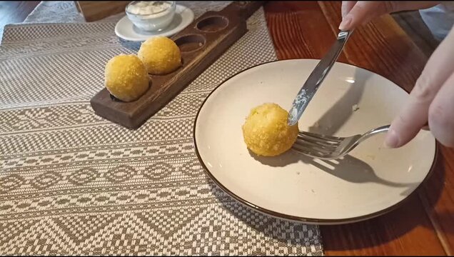 Crispy cheese balls served on plate on wooden table in cozy restaurant setting. Close-up of female hands using cutlery during lunch.