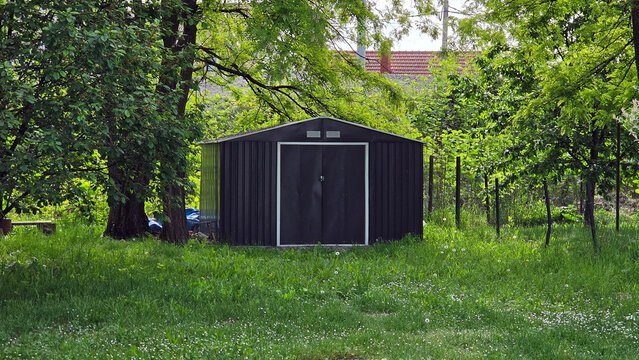 Modern anthracite metal garden shed nestled among lush green trees in a backyard