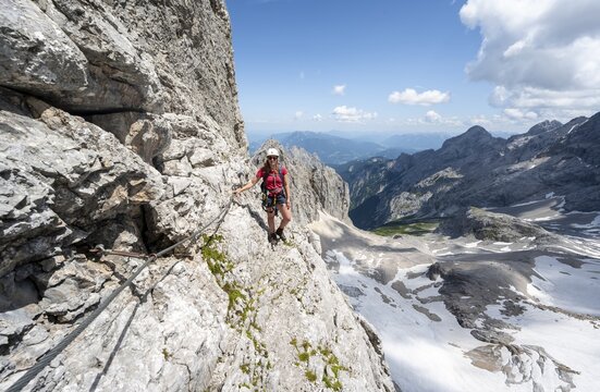 Mountaineer with helmet in a secured via ferrata, Zugspitz via ferrata, ascent to the Zugspitze, view of mountain basin with snowfield of the H&ouml;llentalferner and H&ouml;llental, Wetterstein range, Bavaria, Germany