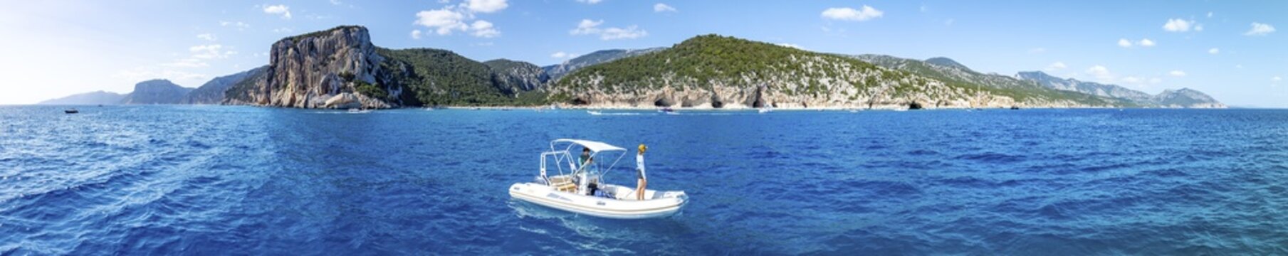 Motor boat off picturesque rocky coast, cliffs and Cala Luna beach, aerial view, Golfo di Orosei, Baunei, Sardinia, Italy