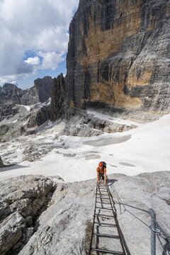 Mountaineer climbs on a ladder in the Via Ferrata Brentari via ferrata, spectacular mountain landscape with steep rock faces, remains of the Vedretta d'Ambiez glacier in the back, Brenta Mountains, Brenta-Adamello Nature Park, Trentino, Italy