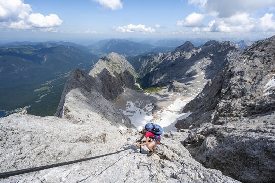 Mountaineer with helmet in a secured via ferrata, Zugspitze via ferrata, ascent to the Zugspitze, view of mountain basin with snow field of the H&ouml;llentalferner and H&ouml;llental, Wetterstein range, Wetterstein range, Bavaria, Germany