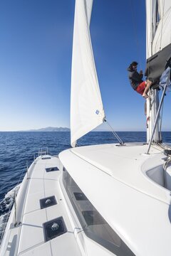 Sailor adjusts the sails on the mast, sailing catamaran sailing, South Aegean Sea, Greece