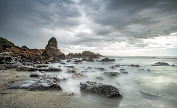 Rocky coast, rocks on the beach, dark rain clouds, long time exposure, West Coast, South Island, New Zealand