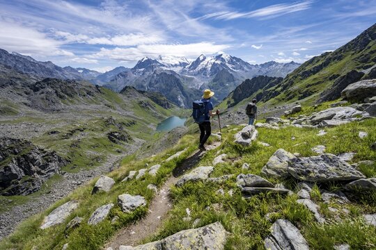 Mountaineer on hiking trail in mountain landscape, descent at Col du Louvie, view of mountain lake Lac du Louvie and glaciated mountain peaks of the Grand Combine, Valais Alps, Val de Bagnes, Valais, Switzerland