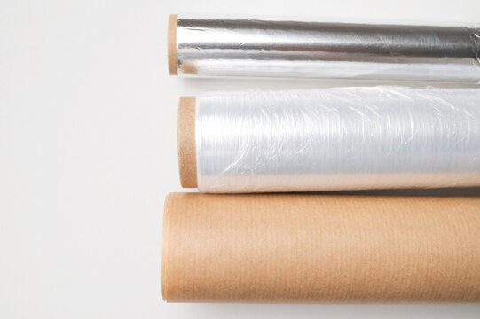Three rolls of kitchen packaging materials on gray background, flat lay top view. Plastic cling film, aluminum foil, baking paper (parchment)