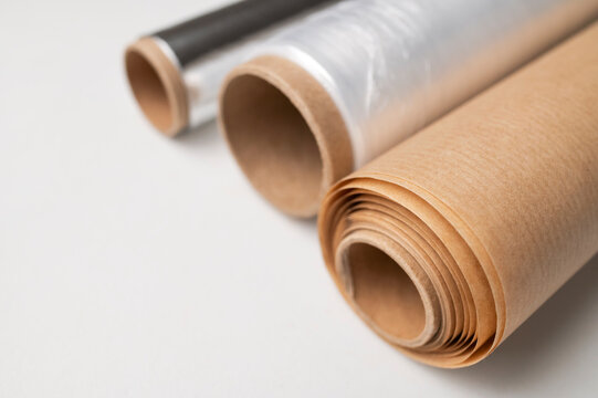 Three rolls of kitchen packaging materials on gray background, flat lay top view. Plastic cling film, aluminum foil, baking paper (parchment)