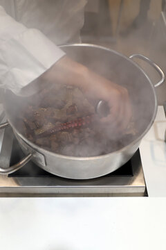 chef cocinando guiso de carne con pulpo en una olla en el fog&oacute;n de la cocina