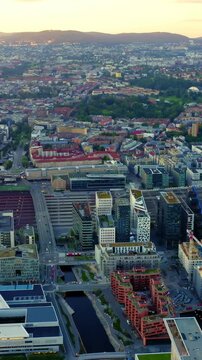 Vertical video. Oslo, Norway. The Oslo Opera House and Barcode skyline rising from the Bjorvika waterfront, aerial panoramic view at sunset with warm light over the fjord and modern city center.. Dro