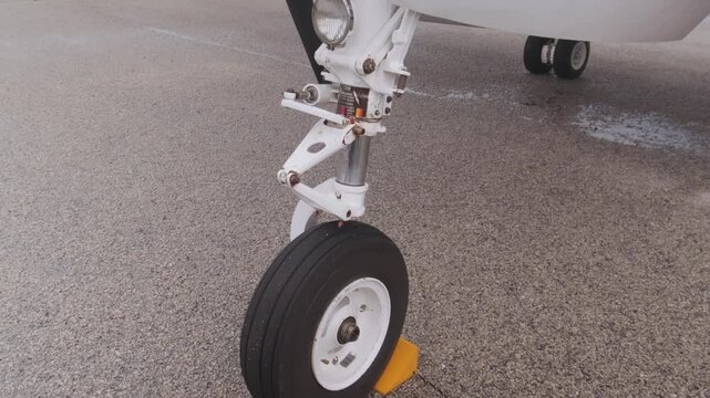 Close-up of airplane front landing gear wheel secured on airport tarmac, showcasing aviation safety procedures, aircraft engineering and ground handling operations.