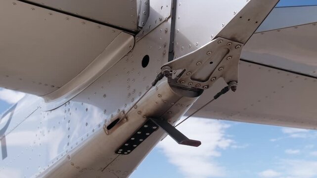 Close-up underside view of airplane tail, wing flap and mechanical hinge system during maintenance inspection, showcasing aviation engineering and aircraft structural components. Anti tail strike
