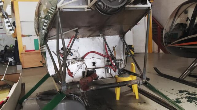Empty helicopter engine compartment in maintenance hangar, missing powerplant revealing internal mounting structures and avionics components during repair work