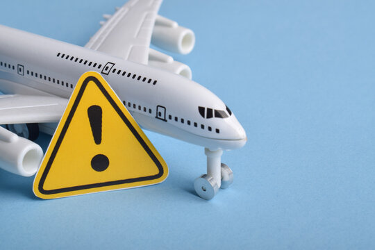 Toy airplane beside a yellow warning sign on blue background representing aviation safety, flight risk, travel alerts, air transport issues, turbulence, delays, and airline warning concept.