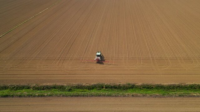 Agricultural tractor plows a large, fertile field, creating neat rows in the freshly tilled earth, captured from a high aerial perspective.