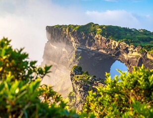 Fototapeta premium Scenic Coastal Cliff With Natural Rock Arch And Green Vegetation Under Bright Sunlight With Morning Mist And Blue