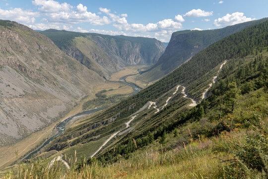 Panoramic view from Katu-Yaryk Pass over the Chulyshman River canyon with winding dirt road, steep cliffs and taiga slopes, Altai Republic, Russia