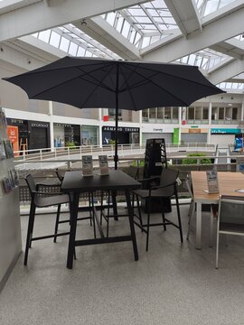 Royan, France - May 10, 2026: E.Leclerc. Black patio umbrella shading a modern outdoor dining table with chairs in a shopping mall interior featuring retail shops