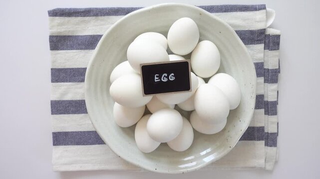 Woman's hand and a ceramic bowl with white eggs on a striped kitchen napkin. Healthy eating, keto and paleo diet concept. High-protein foods. Ideal for nutrition, cooking and dietary lifestyle content