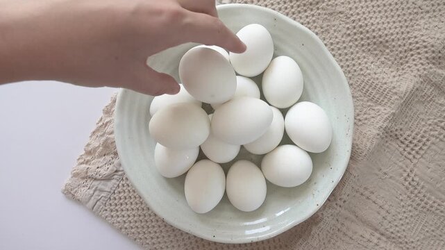 Woman's hand and a ceramic bowl with white eggs on a striped kitchen napkin. Healthy eating, keto and paleo diet concept. High-protein foods. Ideal for nutrition, cooking and dietary lifestyle content