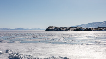Wide winter landscape of frozen Lake Baikal with drifting ice and snow, rocky cape and distant mountains under clear sky, Maloe More strait, Irkutsk Oblast, Russia © TravelFlow