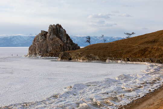 Winter landscape with Shamanka Rock on the frozen surface of Lake Baikal near Khuzhir, Irkutsk Oblast, Russia, with snow, ice patterns and distant mountains