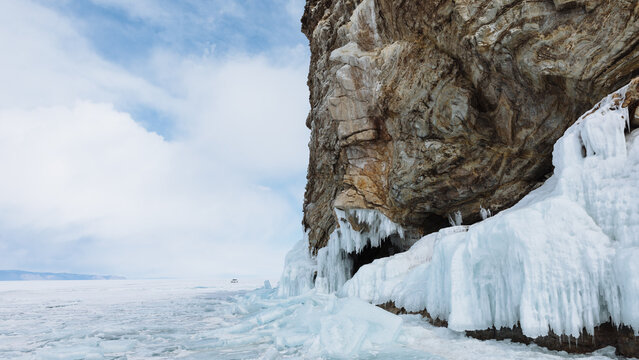 Dramatic winter landscape with icicles and blue ice on a rocky cliff above the frozen shoreline of Lake Baikal, Siberia, Russia, under a cloudy sky