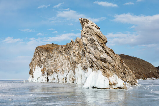 Dramatic rocky cape covered with ice on frozen Lake Baikal near Ogoy Island, Irkutsk Oblast, Russia, winter landscape with clear blue sky and clouds