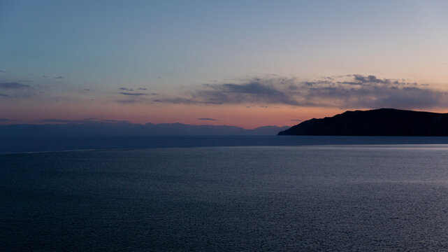 Wide tranquil seascape-like view of Lake Baikal at dusk with distant mountains and calm water near the Angara River source in Listvyanka, Irkutsk Oblast, Russia