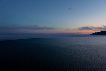Fototapeta premium Wide twilight landscape of the Angara River flowing into Lake Baikal near Listvyanka, Irkutsk Oblast, Russia, with calm water, distant mountains and pastel sky