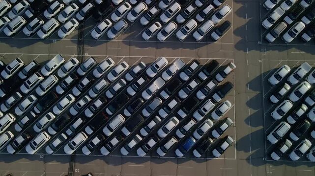 Cinematic drone flight over rows of new cars at a massive parking lot. Automotive industry logistics and vehicle distribution hub.
