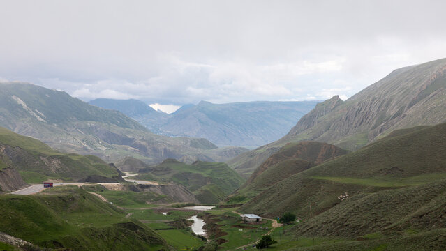 Wide mountain valley with green hills, winding river and rural road under cloudy sky, scenic nature view in Dagestan, North Caucasus, Russia