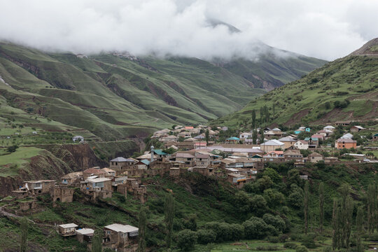 Wide view of Magar village with stone houses on a hillside in a lush mountain valley under low clouds, Republic of Dagestan, Russia, summer travel scenery