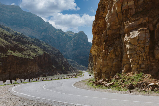 Scenic winding asphalt road through a rocky mountain canyon with dramatic cliffs and clouds, travel route in Dagestan, North Caucasus, Russia on a sunny day