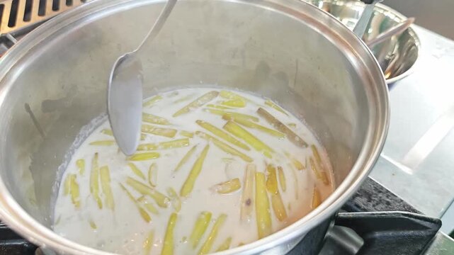 Cooking lotus stalks in hot creamy coconut milk broth with a ladle.