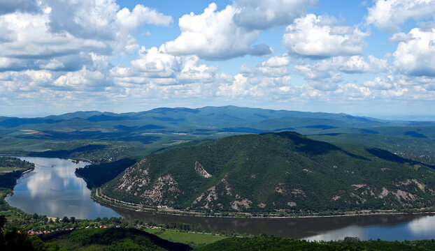 the riverbend of the Danube river at Zebegeny village, and Nagymaros, Hungary. lush green hills in the background. popular summer holiday destination. smooth calm water surface. blue sky, white clouds