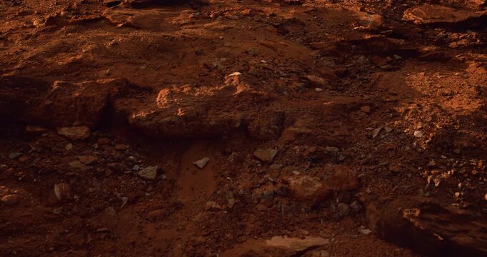 A close-up of dry red desert ground covered in loose dirt, gravel, and scattered rocks in warm earthy tones.