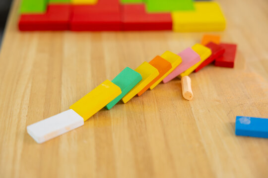 Colorful wooden domino blocks falling in sequence on a wooden table, educational toy concept showing chain reaction, creativity, learning, and problem solving.
