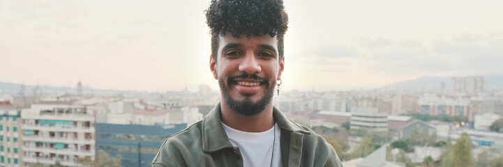 Naklejka premium Close-up of smiling young guy posing at the camera while standing on the balcony. Panoramic