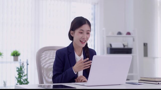 young Asian businesswoman video conference call laptop smiling happy professional office remote work online meeting cheerful presentation white modern