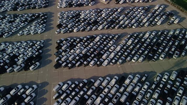 Cinematic drone flight over rows of new cars at a massive parking lot. Automotive industry logistics and vehicle distribution hub.