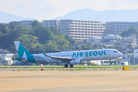 Fukuoka Japan - 2025 August 14: An Air Seoul Airbus A321 (HL7212) taxiing on the runway after landing at Fukuoka Airport with buildings and mountains in the background.