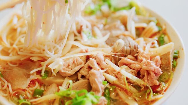 Detailed close up of traditional Bun Bo Hue featuring rice vermicelli noodles, tender beef slices, and fresh green onions in a rich, spicy broth