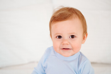 Fototapeta premium Baby close-up portrait, smiling and joyful little child on a white bed in a blue bodysuit