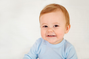 Fototapeta premium Baby close-up portrait, smiling and joyful little child on a white bed in a blue bodysuit