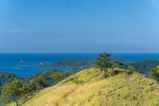A beautiful landscape of Riung Seventeen Islands in Flores, Indonesia, featuring golden savanna hills overlooking the blue sea and archipelago.
