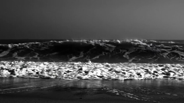 Dramatic monochrome view of ocean waves crashing onto a sandy beach creating a textured foam effect