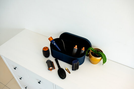 Open navy hair styler case showing tools inside with round barrel brush and hair clip on white dresser, beauty technology and modern hair care organization and storage concept