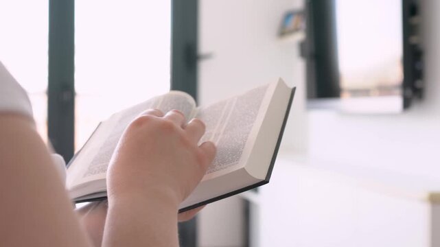 Person, bible book and point with hands, reading or studying for praise, worship or faith in home. Knowledge, closeup and information with religion, learning or spiritual guide for connection to God