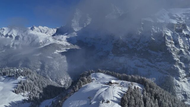 Drone perspective over winter mountains, forested ridge, and cloud shadows in the Bernese Oberland near M&uuml;rren, Switzerland.